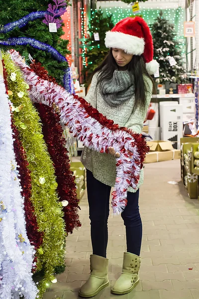 Молода жінка в капелюсі Санта вибирає прикраси на ялинку — стокове фото