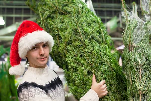 Mladý muž koupí vánoční strom v úložišti — Stock fotografie