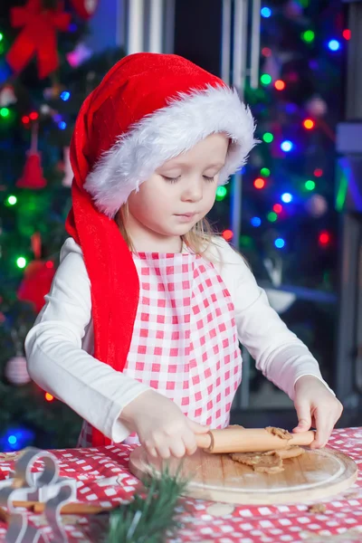 Entzückendes kleines Mädchen mit Weihnachtsmütze, das zu Hause Lebkuchen backt — Stockfoto