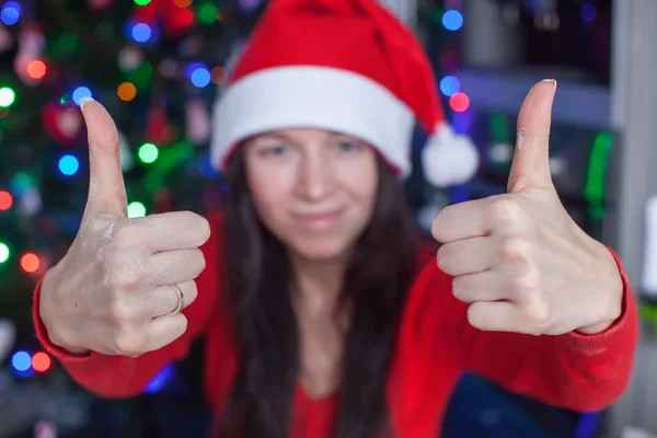 Young woman in Christmas hat raised thumbs up at home — Stock Photo, Image