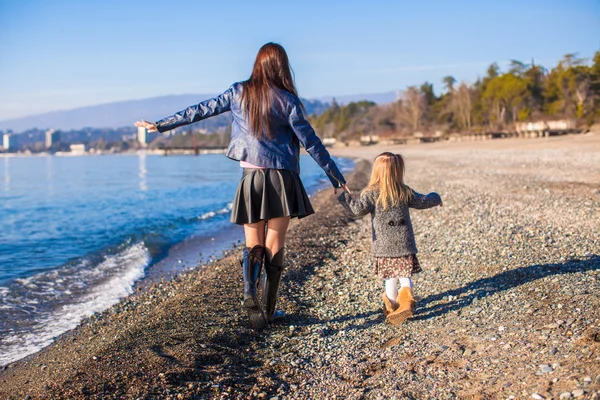 Liten flicka och hennes mamma som promenerar på stranden i solig vinterdag — Stockfoto