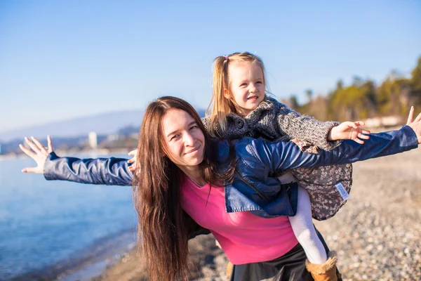 Jonge moeder en schattig dochtertje vliegen als een vogel in winter beach — Stockfoto