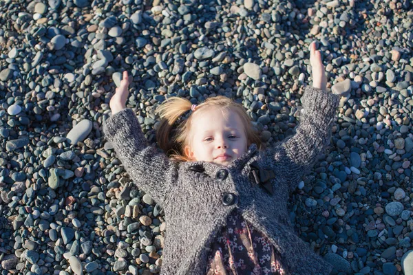 Очаровательная маленькая девочка лежит на пляже в зимний солнечный день — стоковое фото