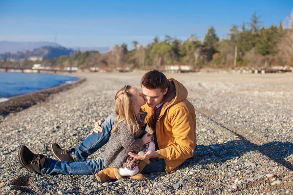 Молодой отец держит маленькую дочь, целующую его на пляже в солнечный день — стоковое фото