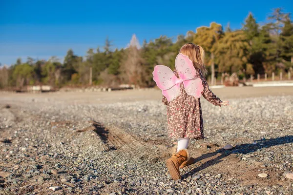 Bedårande liten flicka med butterfly wings kör längs stranden i en solig vinterdag — Stockfoto