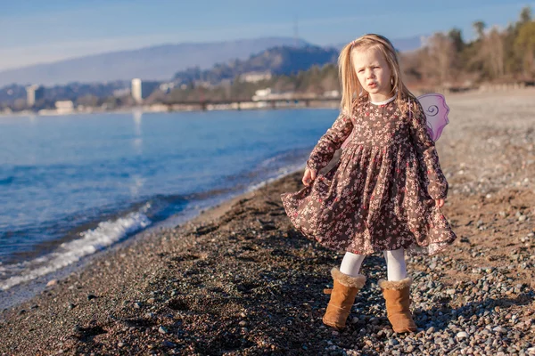 Adorable petite fille avec des ailes de papillon courant le long de la plage par une journée ensoleillée d'hiver — Photo