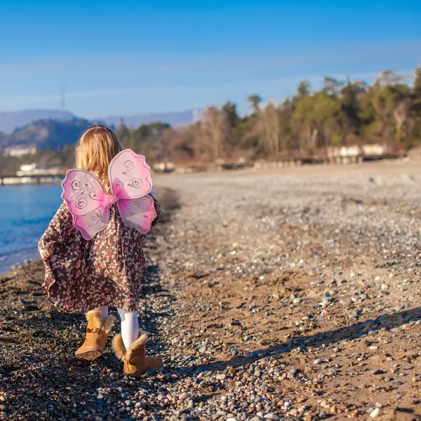 Kleines Mädchen mit Schmetterlingsflügeln läuft an einem sonnigen Wintertag am Strand entlang — Stockfoto