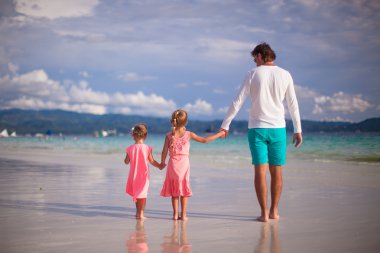 vue arrière du père et les deux filles marchant sur la plage tropicale de blanc