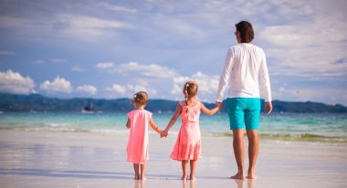 vue arrière du père et les deux filles marchant sur la plage tropicale de blanc
