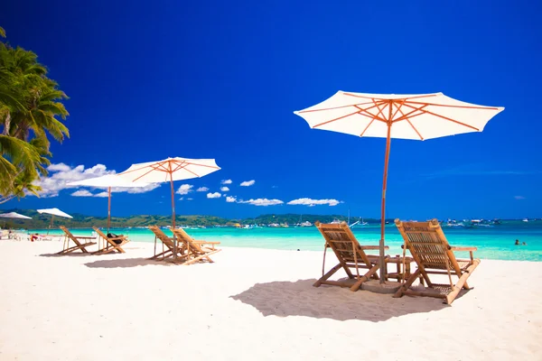 Dřevěné židle a slunečníky na pláži s bílým pískem směrem k laguně — Stock fotografie