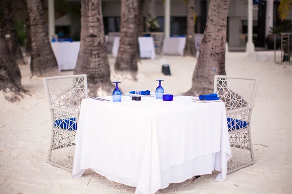 Tarjoillaan Tyhjä ulkoilma pöytä asetettu päivälliselle valkoisella rannalla — kuvapankkivalokuva