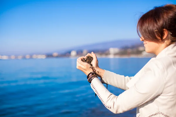 Le mani della donna che tengono piccole pietre formano lo sfondo a forma di cuore il mare — Foto Stock