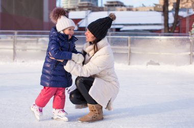 glimlachend jonge moeder en haar schattige kleine dochter ijs schaatsen samen