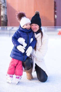 glimlachend jonge moeder en haar schattige kleine dochter ijs schaatsen samen