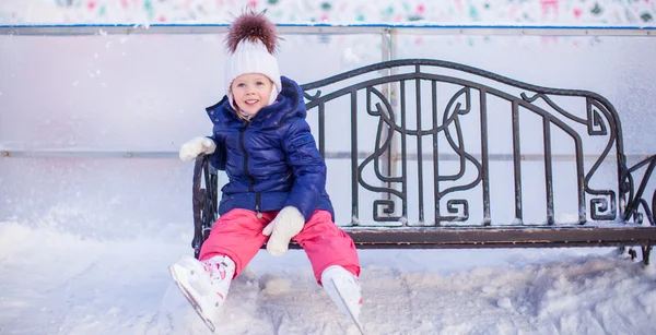 Little girl sitting on a bench in the skating rink — Stock Photo, Image