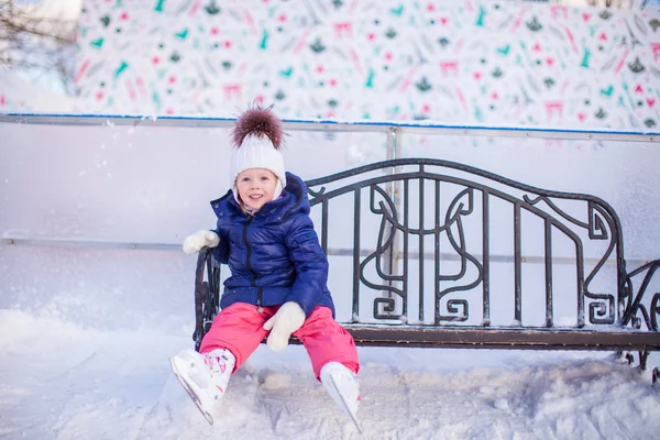 Little girl sitting on a bench in the skating rink — Stock Photo, Image