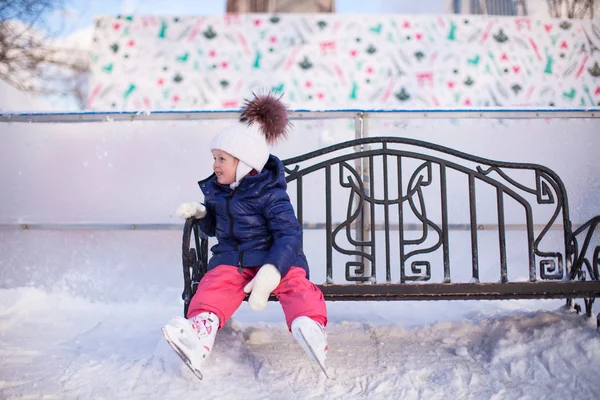 Little girl sitting on a bench in the skating rink — Stock Photo, Image