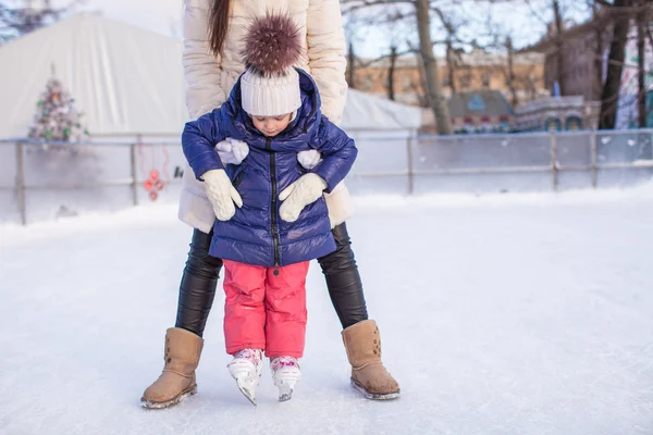 Маленькая очаровательная девочка со своей мамой, которая учится кататься на коньках — стоковое фото