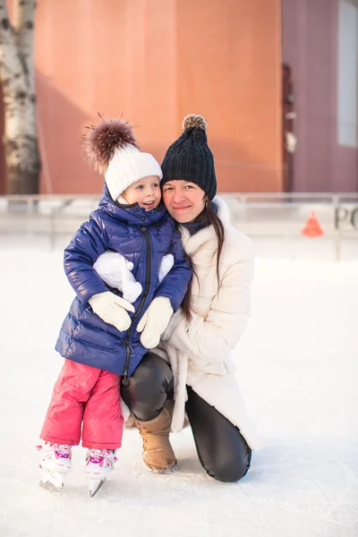 Улыбающаяся молодая мать и ее милая маленькая дочь катаются на коньках вместе — стоковое фото