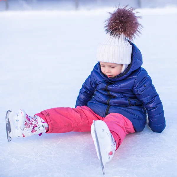 Petite adorable fille assise sur la glace avec des patins après la chute — Photo