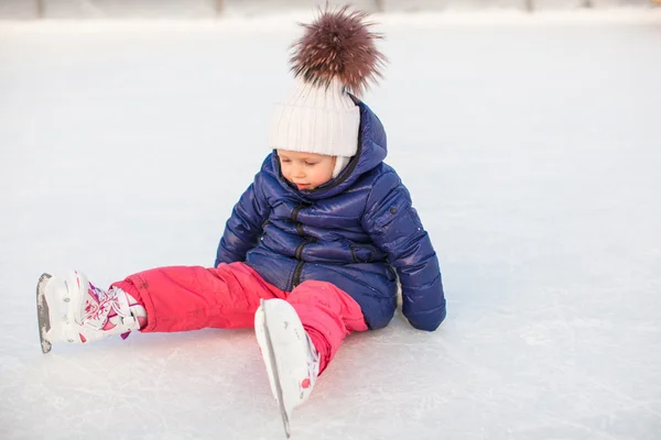 Pequena menina adorável sentado no gelo com patins após a queda — Fotografia de Stock