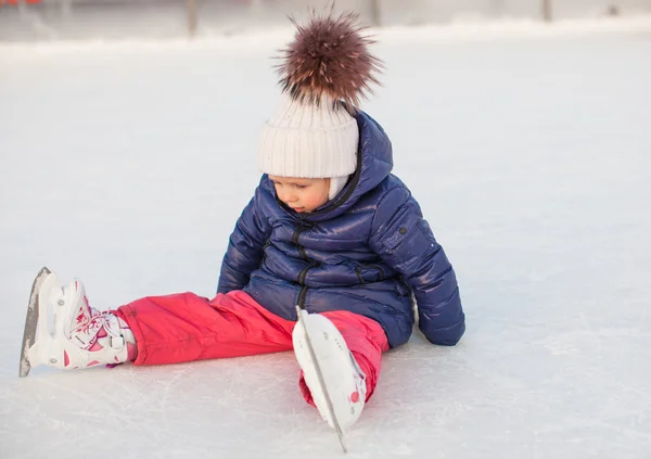 Petite adorable fille assise sur la glace avec des patins après la chute — Photo