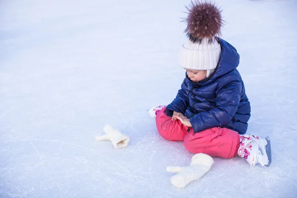 Kleines entzückendes Mädchen sitzt nach dem Sturz mit Schlittschuhen auf dem Eis — Stockfoto