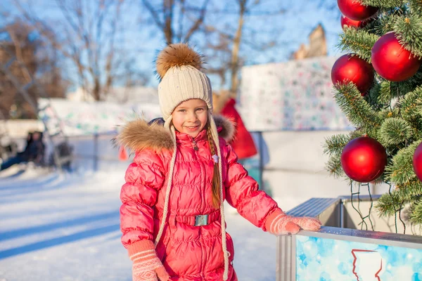 Portrait of adorable little girl near Christmas tree on skating rink — Stock Photo, Image