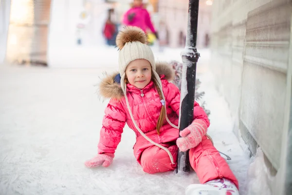 Happy adorable girl sitting on ice with skates after the fall — Stock Photo, Image