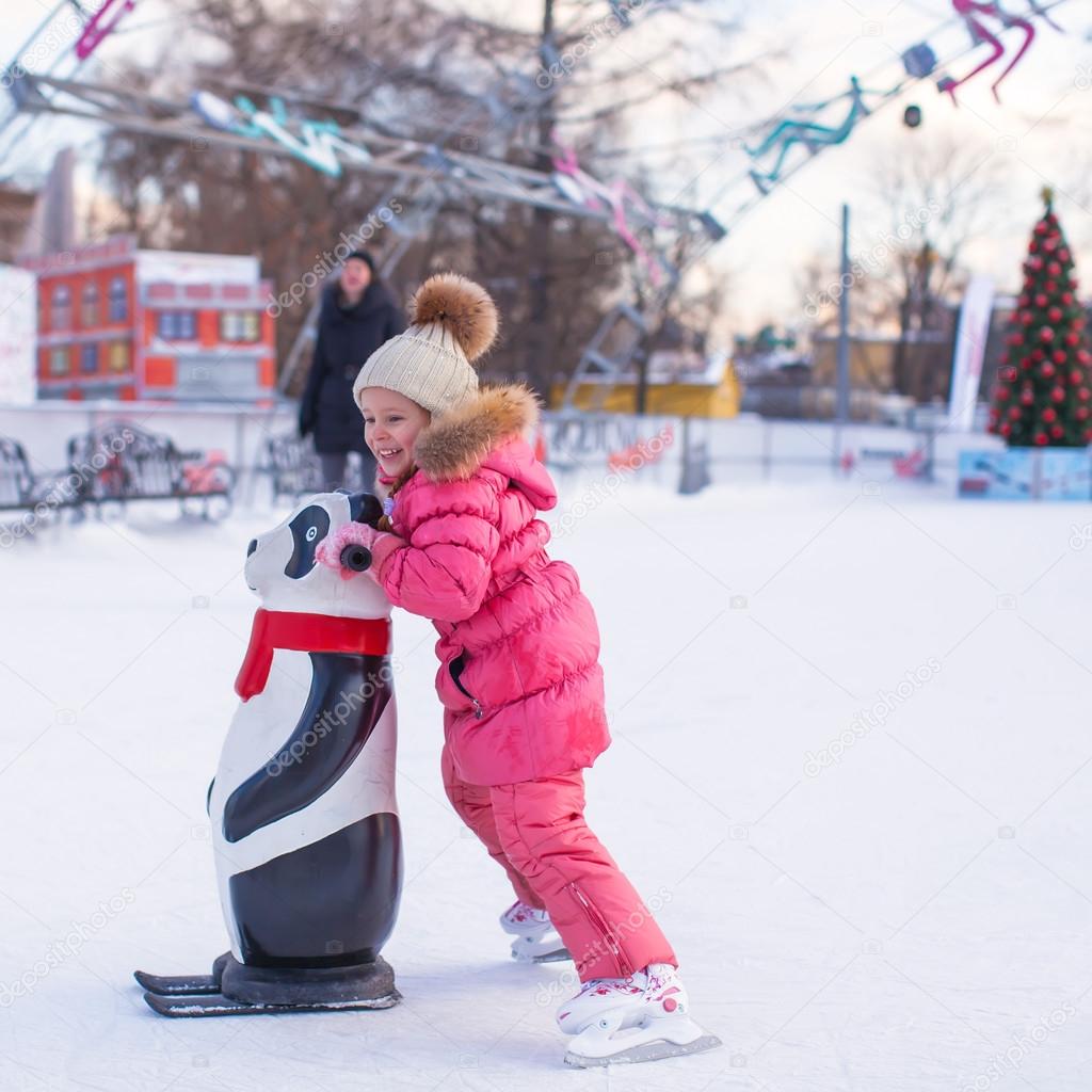 Little cheerful girl learning to skate on the rink