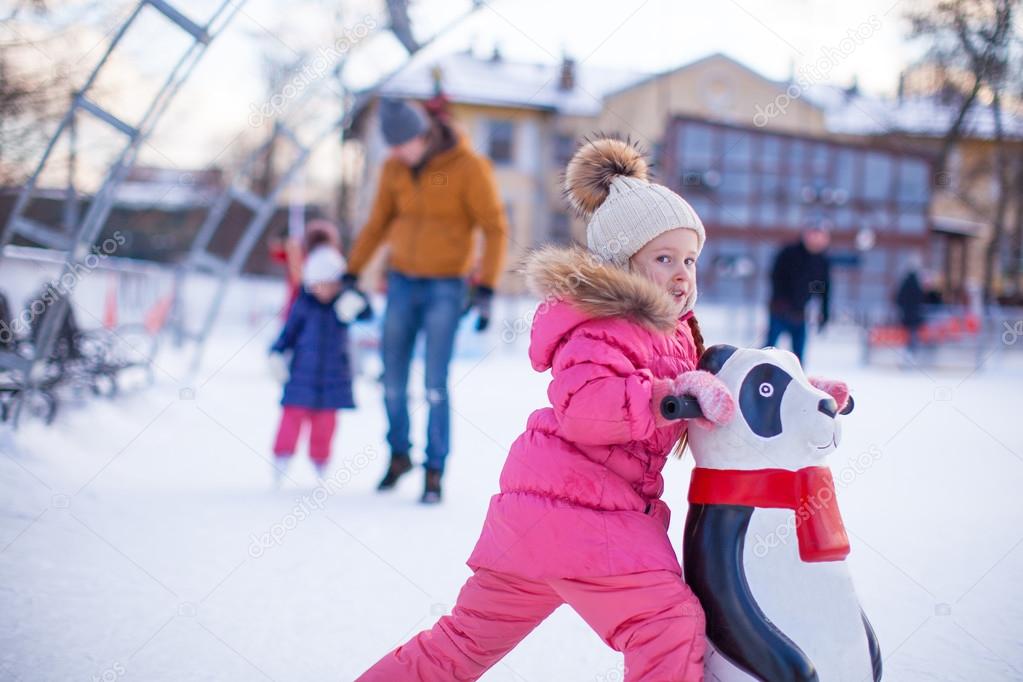 Portrait of adorable girl skating on the ice-rink background her father and little sister