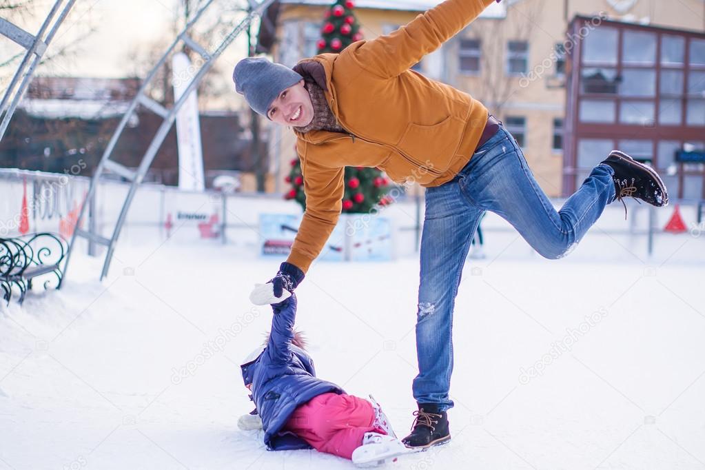 Father with his daughter skates on ice skating in the winter.
