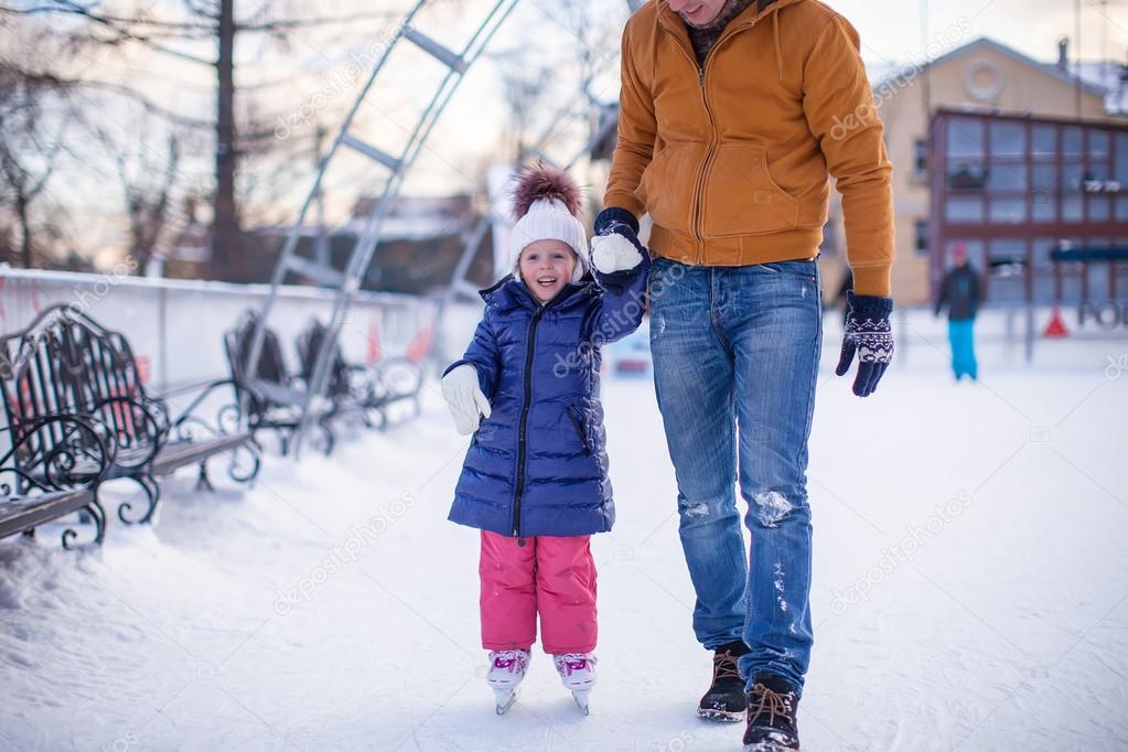 Closeup of adorable little girl with young dad on skating rink
