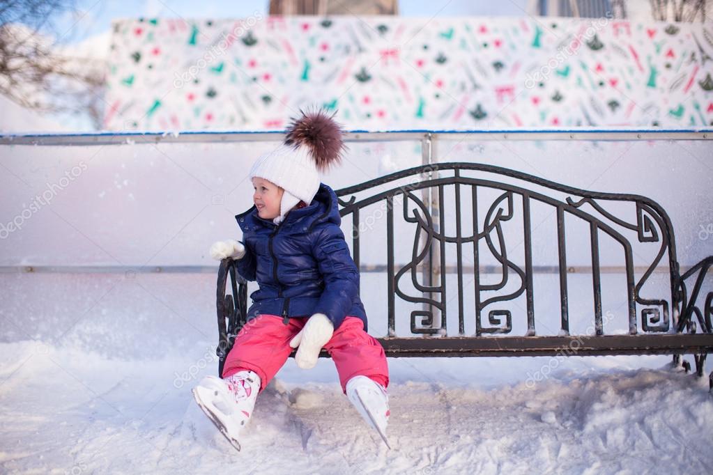 Little girl sitting on a bench in the skating rink
