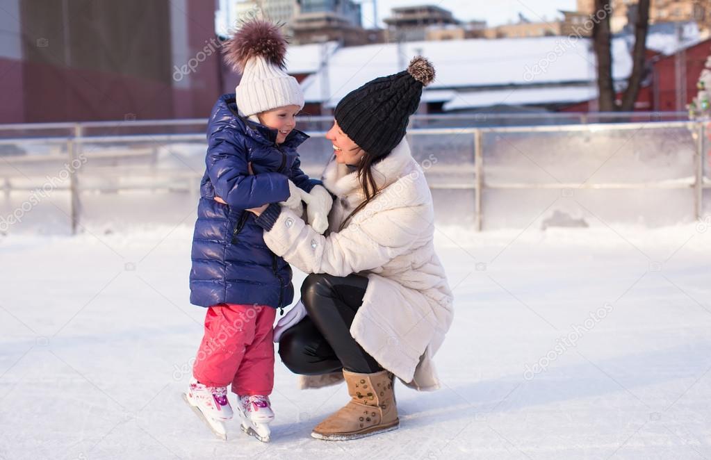 Young mother and her cute little daughter on a skating rink