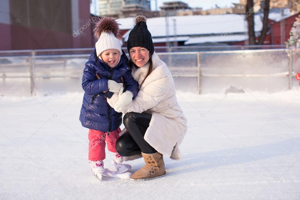 Smiling young mother and her cute little daughter ice skating together