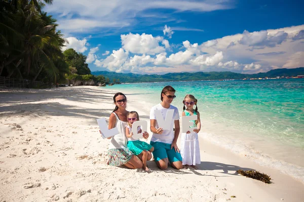 Young happy family of four on tropical vacation with word LOVE — Stock Photo, Image