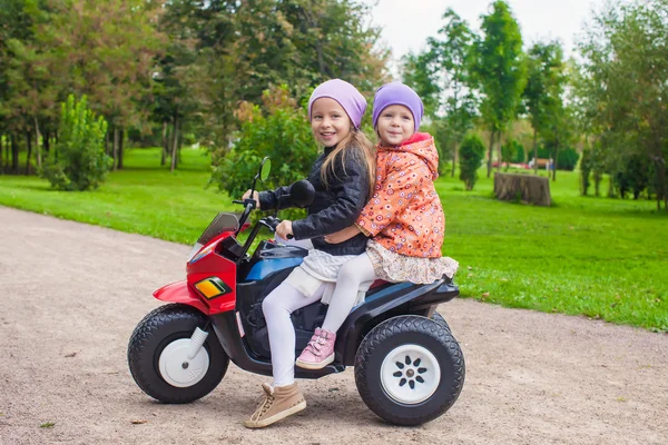 Mały śliczny siostry siedzi na motocykl zabawka zielony Park — Zdjęcie stockowe