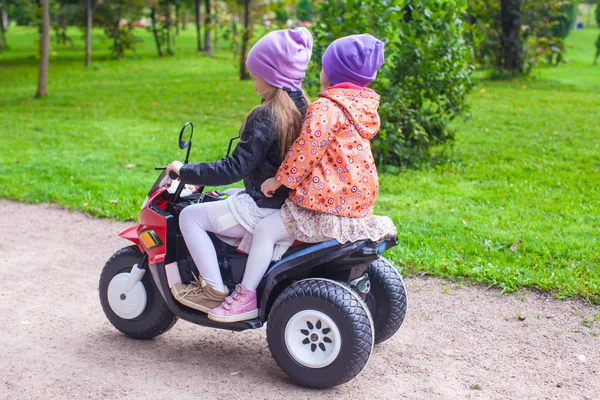 Little adorable sisters sitting on bike in green park — Stock Photo, Image