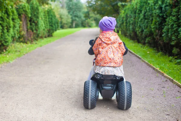 緑豊かな公園でバイクの愛らしい小さな女の子に乗るの背面します。 — ストック写真