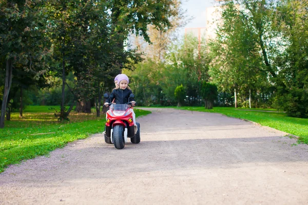 Adorable little girls riding on kid's motobike in the green park — Stock Photo, Image