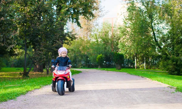 愛らしい女の子、緑豊かな公園の子供の motobike に乗る — ストック写真