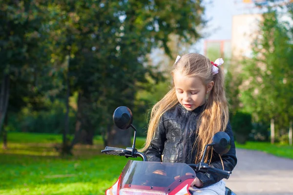 Adorable happy little girl in leather jacket sitting on her toy motorcycle — Stock Photo, Image