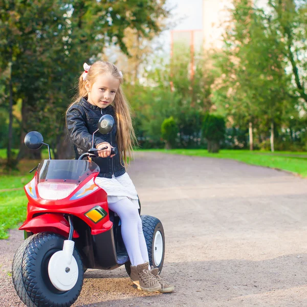 Pequeña chica de roca adorable en chaqueta de cuero sentada en su motocicleta de juguete —  Fotos de Stock