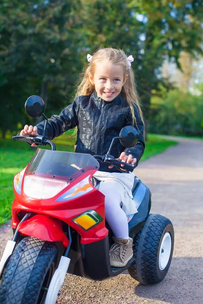 Adorable happy little girl in leather jacket sitting on her toy motorcycle — Stock Photo, Image