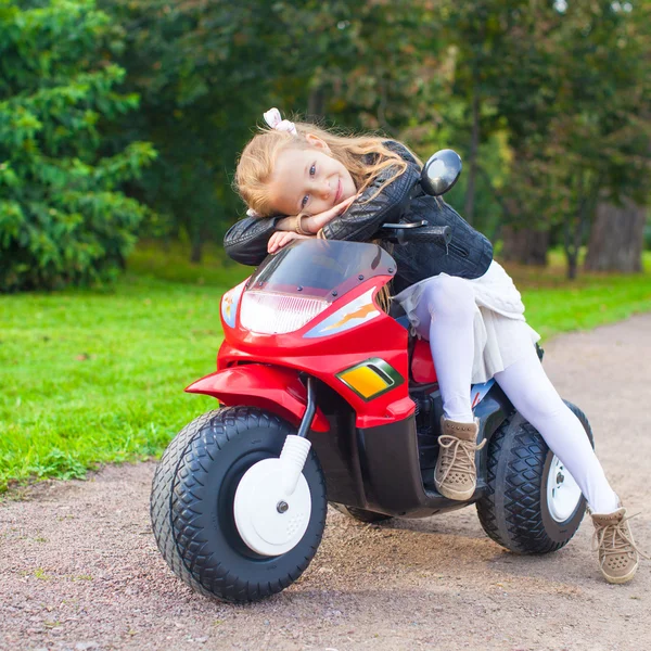 Adorable niña feliz en chaqueta de cuero sentada en su motocicleta de juguete —  Fotos de Stock