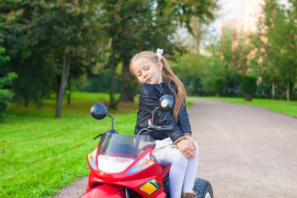 Adorável bonito menina em jaqueta de couro sentado em sua motocicleta de brinquedo fora — Fotografia de Stock