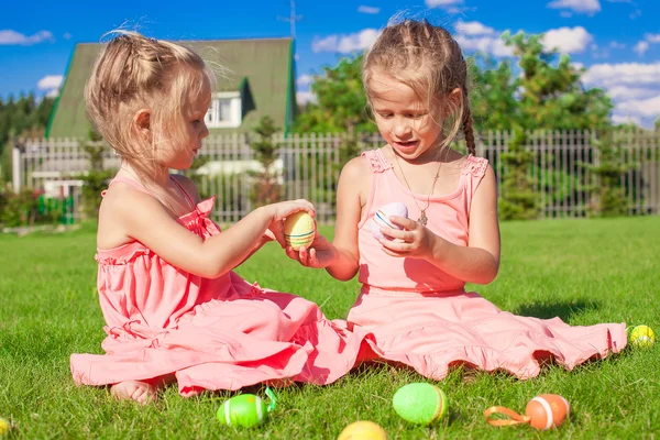Очаровательные маленькие девочки играют с пасхальными яйцами на зеленой траве — стоковое фото