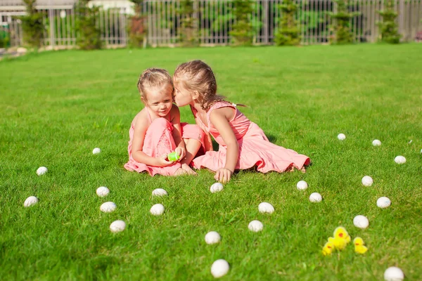 Oudere zus kussen jongere op een groene glade van Pasen eieren — Stockfoto