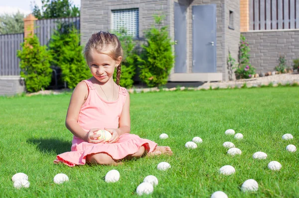 Kleines Mädchen spielt mit weißen Ostereiern im Hof — Stockfoto